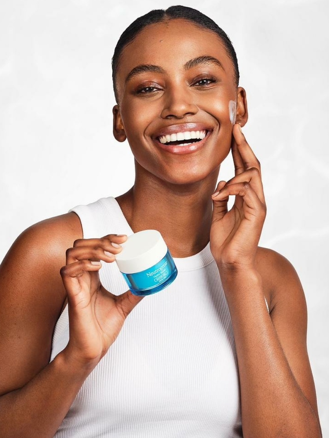 Black model in a skincare campaign holding a moisturiser, clean studio shot