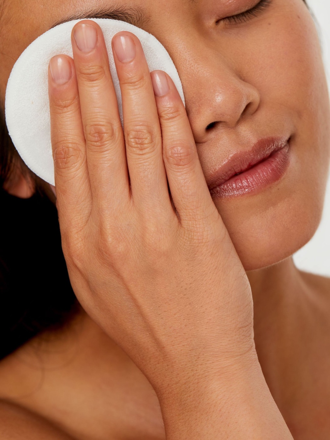 A hand model holding a cotton pad to the face in a beauty shot