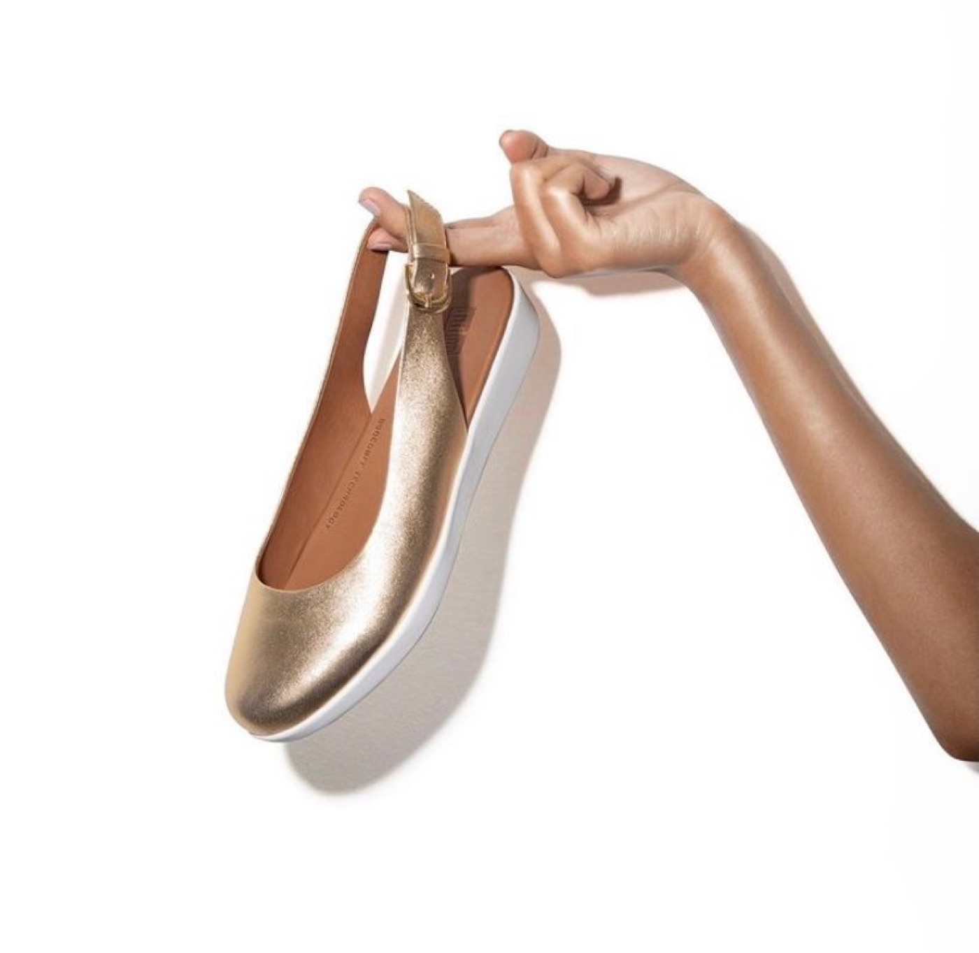 A hand model holding a gold shoe against a white background