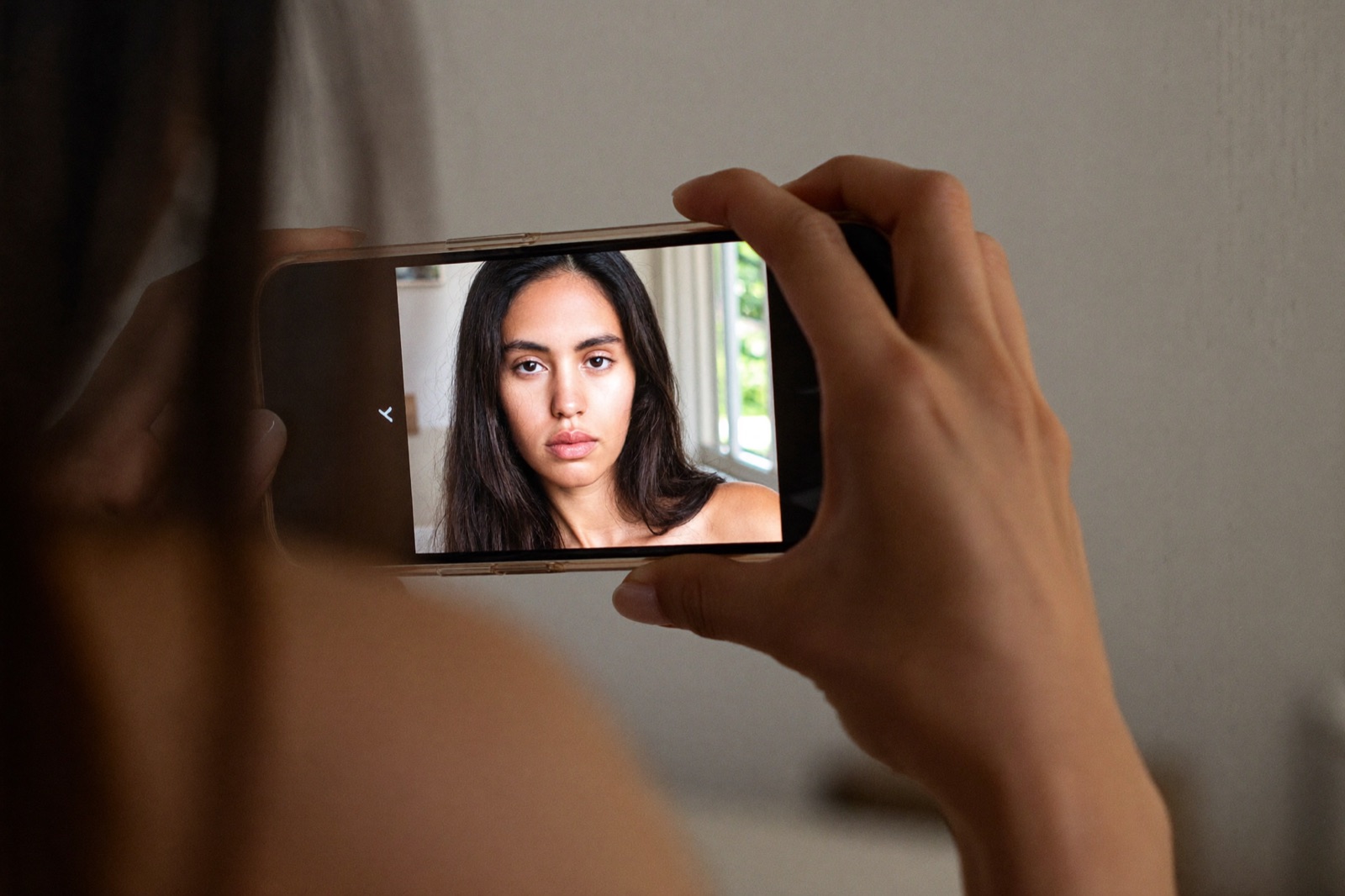Close crop of a model's hands holding a phone, reviewing a simple daylight self-portrait on screen