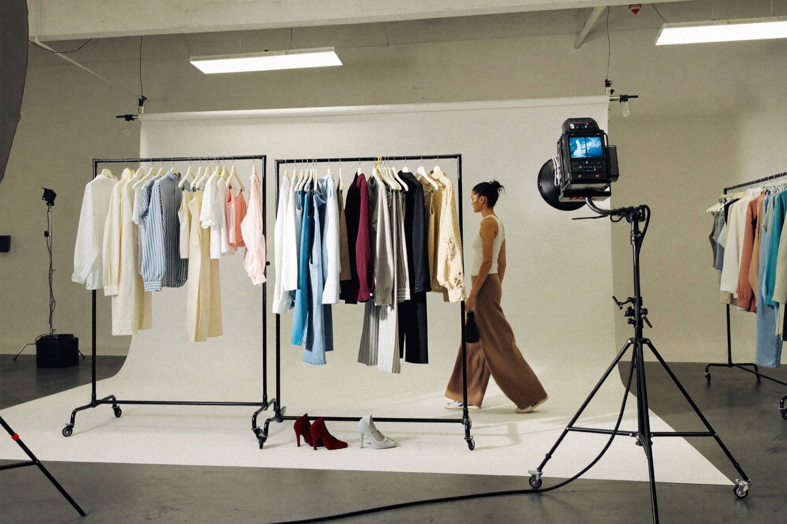 A model mid-change on an e-commerce shoot set, rail of clothing visible behind, plain white backdrop and studio lighting