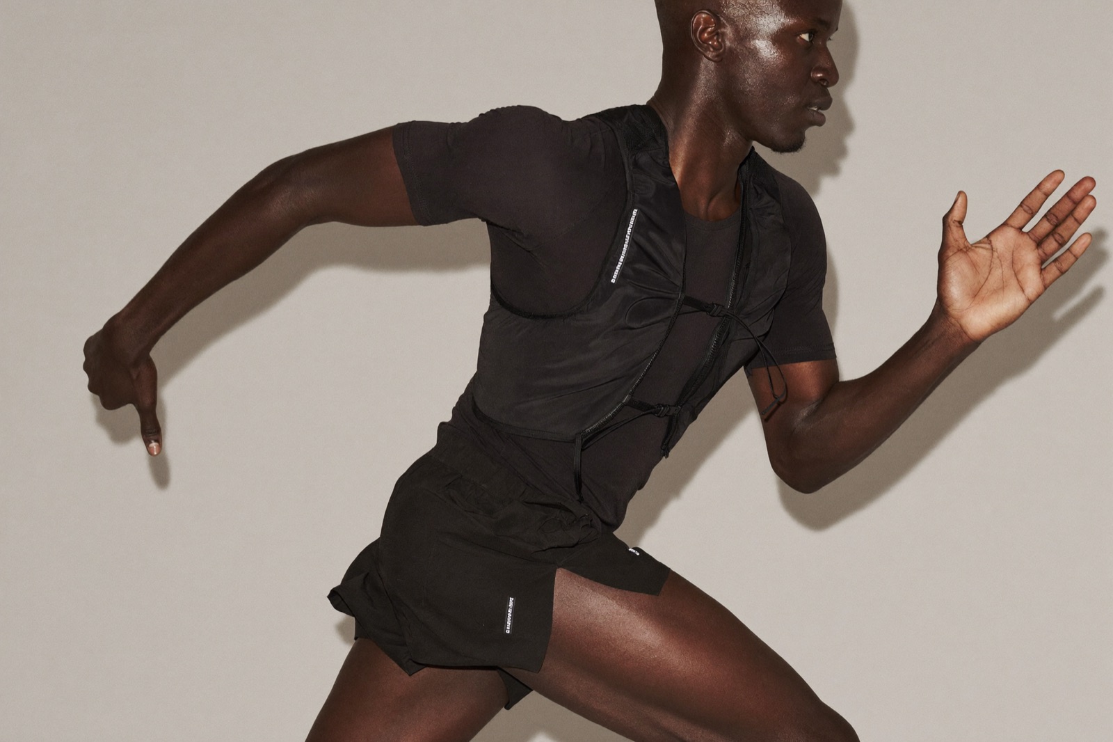 A model mid-stride in running kit against a plain studio backdrop, natural expression, one arm caught in motion blur