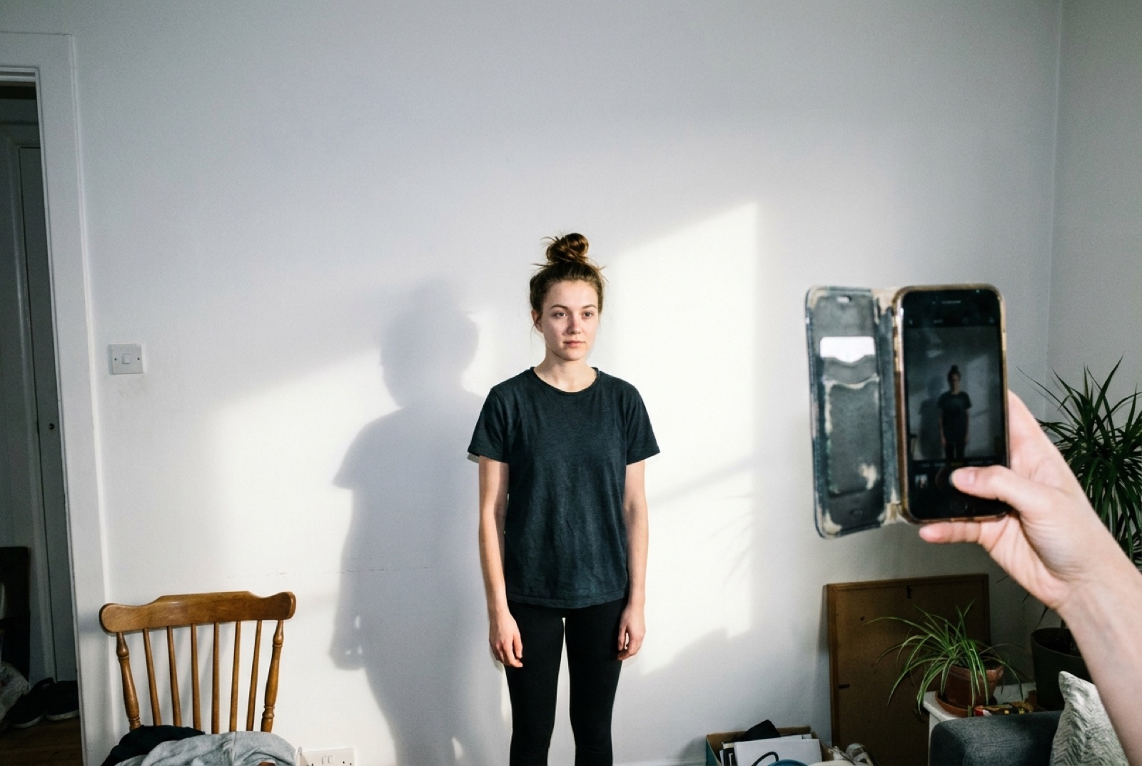 A new applicant having phone digitals taken at home against a plain wall in natural daylight