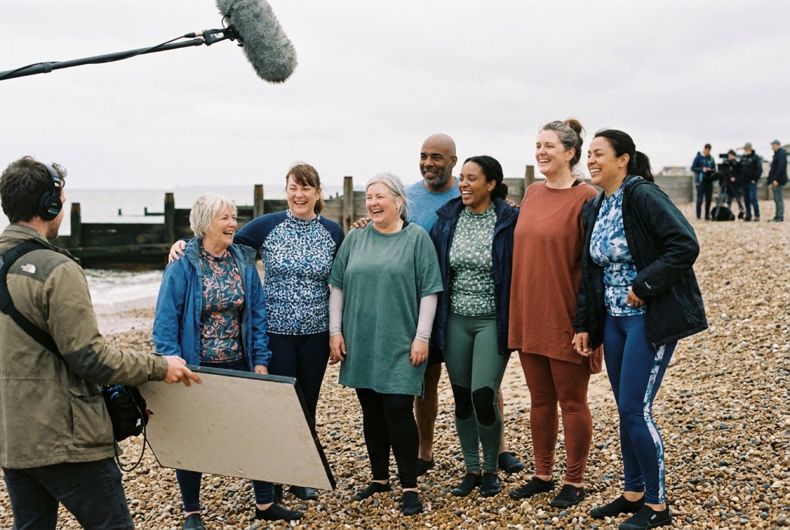 A diverse group of models of different body shapes and ages in beachwear laughing together on a British beach during a campaign shoot